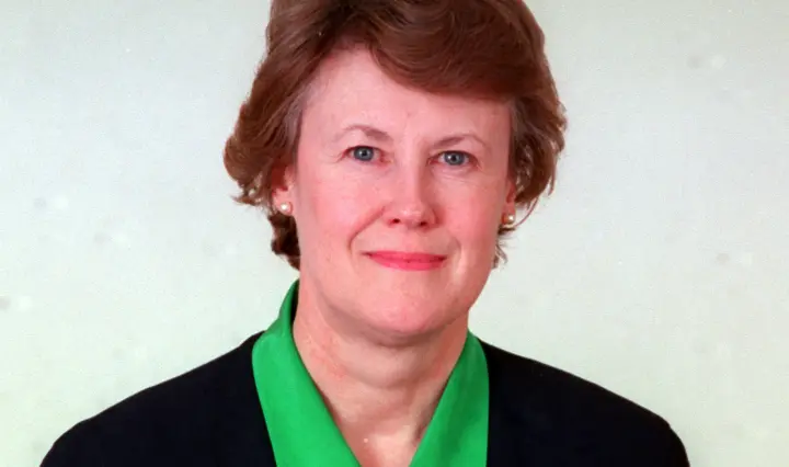 Judith Chaplin, head and shoulders photo with red hair wearing a bright green blouse and black jacket.