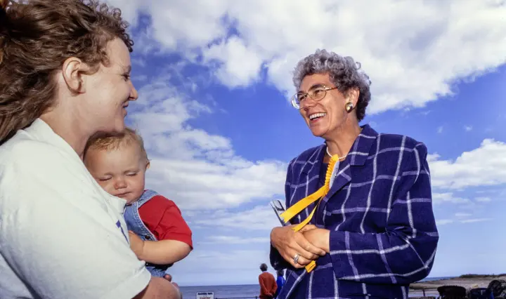 Diana Maddock smiling and talking to a woman holding a baby