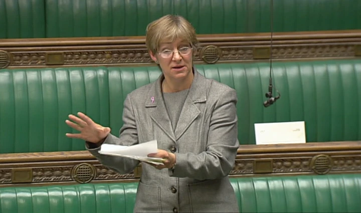 Rachel Squire wearing a grey suit standing with backdrop of green benches